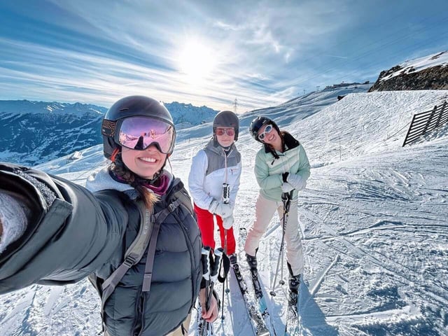 Three people in ski gear pose for a selfie on the ski slopes in Switzerland