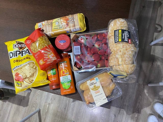 A table filled with groceries such as eggs, chicken, strawberries, dry pasta, pasta sauce, Doritos tortilla chips, and shampoo