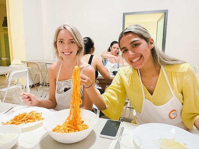 Two students with bowls of pasta in front of them at a cooking class in Florence, Italy