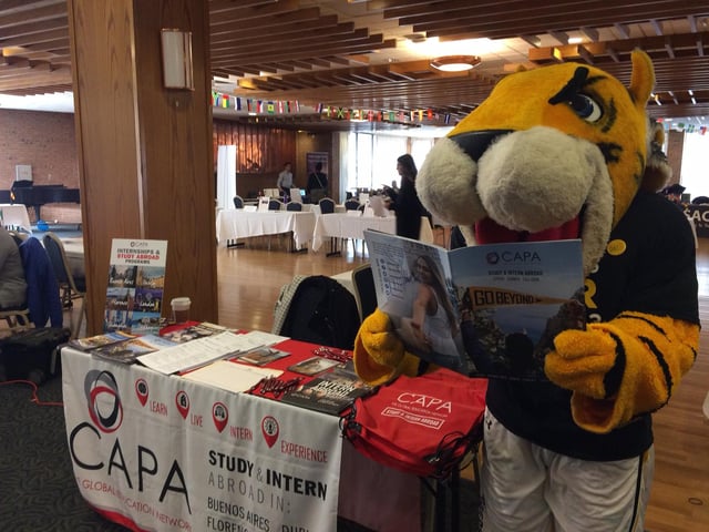 university mascot reading a CAPA brochure next to our booth at a study abroad fair on campus