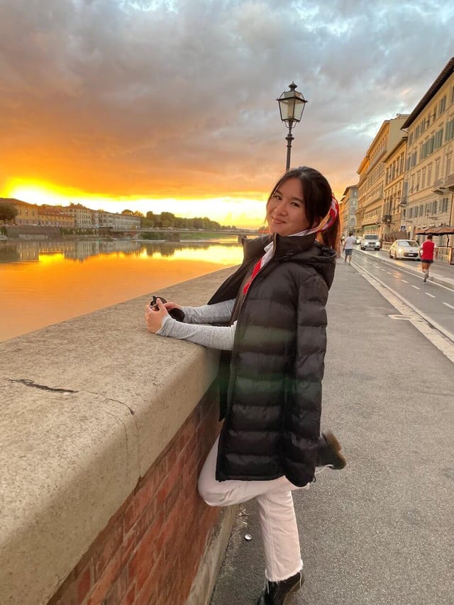 Lynn Dang smiling and standing on a bridge by the Arno River during sunset in Florence
