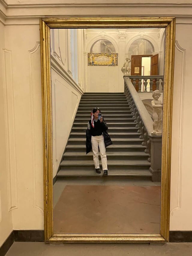 Student taking a photo of themselves with a floor-length mirror at the CAPA Florence Center with stairs in the back