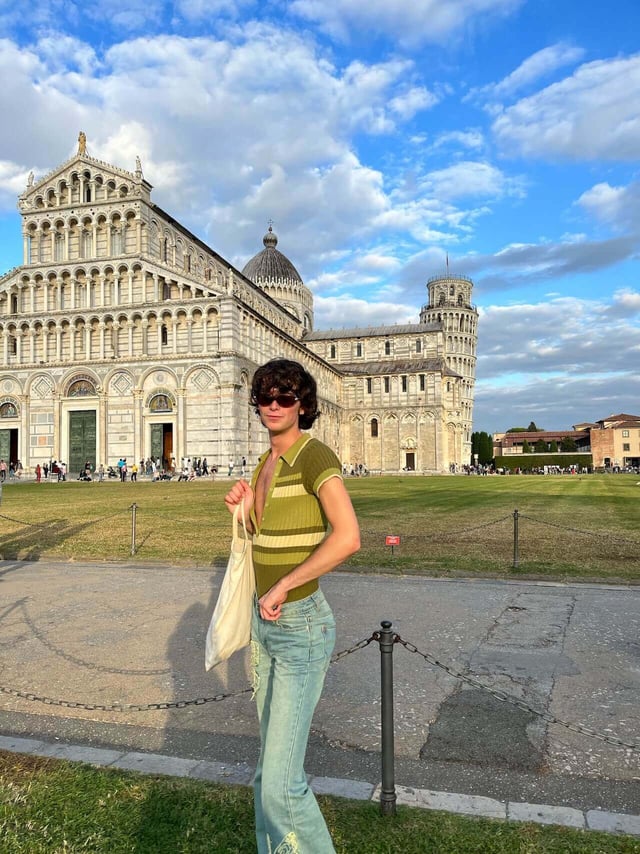 A person standing on the grass with an Italian architectural building in the back