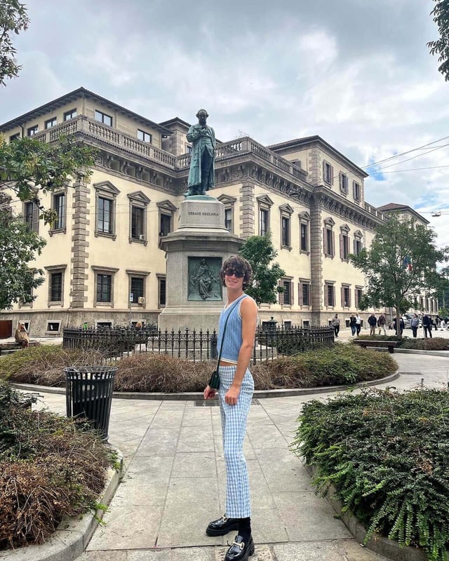 A fashionable person posing in front of a statue outdoors at Milan Fashion Week