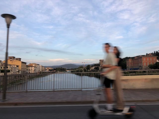 A couple crossing the Arno River bridge on an electric scooter