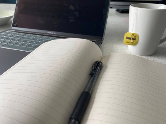 A blank journal with a laptop and mug in the back