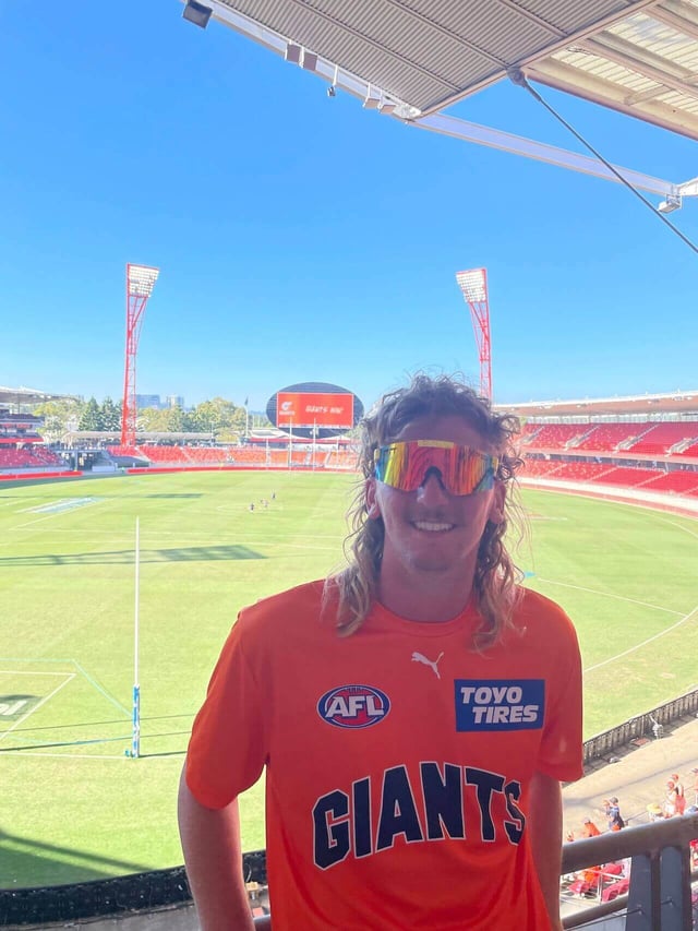 A person wearing sunglasses and smiling in a GWS GIANTS t-shirt while at the GIANTS stadium in Sydney
