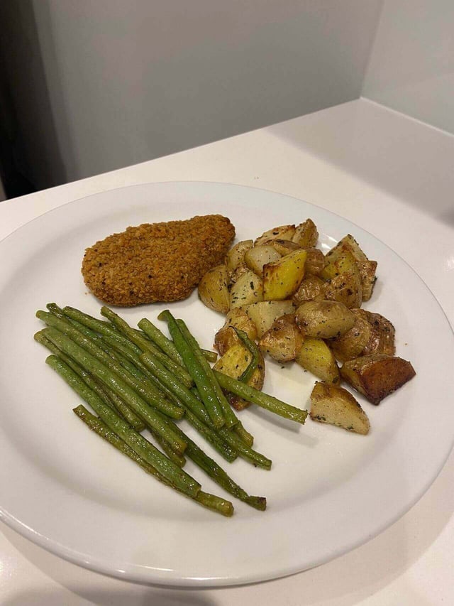 A dinner dish with a breaded cutlet, potatoes, and beans