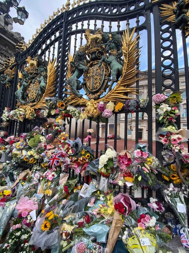 Buckingham Palace gates filled with flowers, cards, and photos from the public