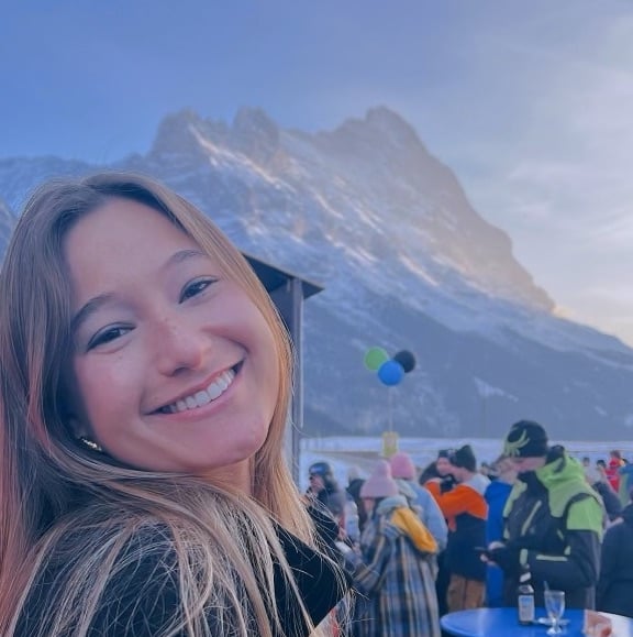 A student smiling at a ski festival in Switzerland with a crowd in the back and a snowcapped mountain
