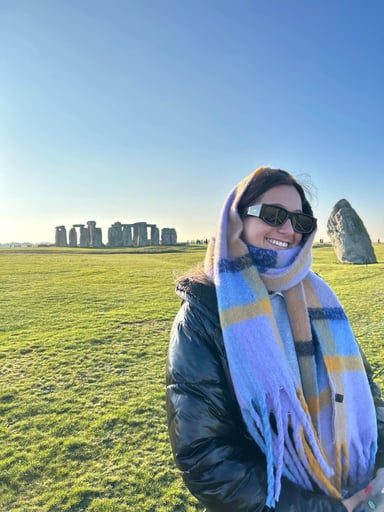 A person wearing sunglasses, scarf, and a coat standing in front of Stonehenge